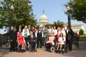 Group of AAPD interns standing or sitting in wheelchairs with the Capitol Building in the background